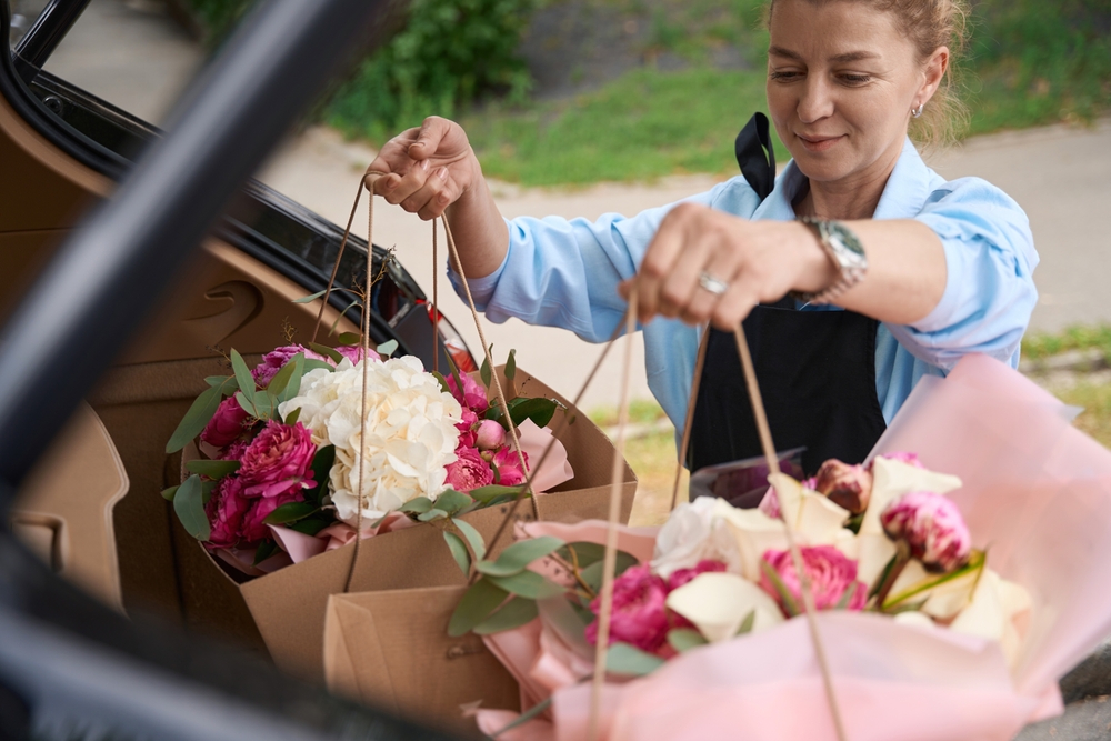 Florist,puts,packages,with,bouquets,of,flowers,in,car,trunk